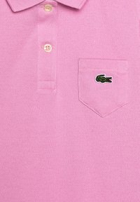 Růžové polo tričko s texturovanou pleteninou, límečkem na dva knoflíky a malým vyšitým zeleným krokodýlem na kapse.