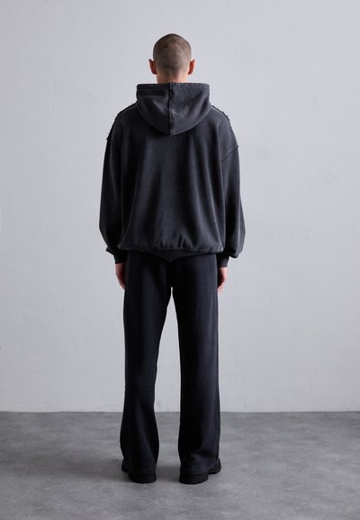 Hætte sweatshirt i mørkegrå bomuld med slidte detaljer, oversized pasform og matchende mørke bukser, vist fra bagsiden.