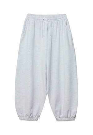 Osoba w pasiastym krótkim topie i luźnych, jasnoszarych spodniach dresowych, jedna ręka unosi top, druga trzyma spodnie dresowe.