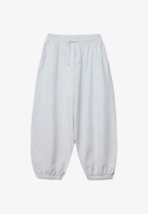 Person trägt ein gestreiftes Crop-Top und lockere hellgraue Jogginghosen, eine Hand hebt das Top an, die andere hält die Jogginghosen.