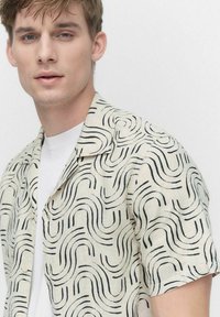 Korte mouwen, lichtbeige shirt met een zwart golvend patroon. Button-down kraag, relaxte pasvorm, gemaakt van lichtgewicht stof.