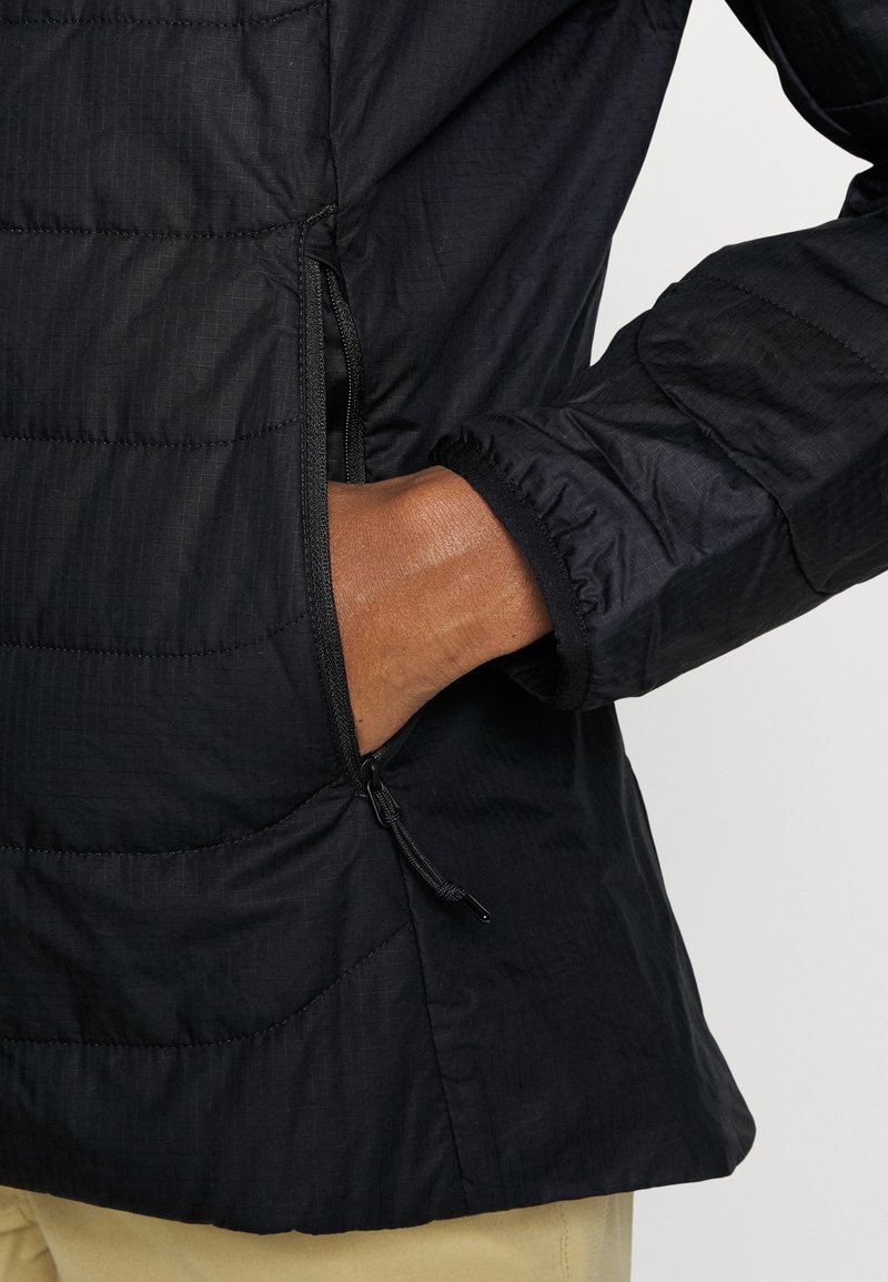 Schwarze Steppjacke mit einer Reißverschlusstasche, elastischen Bündchen und genähten Paneelen. Der Stoff hat eine glatte, leichte Textur.