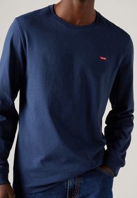 Granatowa koszulka z długim rękawem wykonana z bawełny, z okrągłym dekoltem i małym czerwonym logo Levi's na piersi. Miękka faktura, dopasowany fason.
