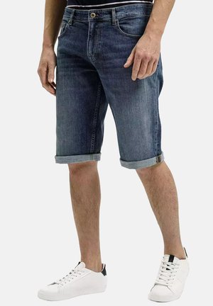 Dżinsowe szorty w ciemnym odcieniu, z podwiniętym dołem, pięcioma kieszeniami i metalowym zapięciem na guzik. W zestawie z białymi trampkami.