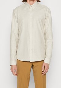 Lichtbeige overhemd met lange mouwen en knoopsluiting, voorzien van een kraag, gemaakt van een gestructureerd materiaal. Heeft een zeven knopen tellende voorkant en een afgeronde zoom.