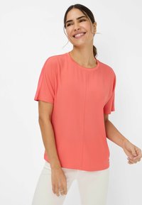 Coral pink short-sleeve top in lightweight fabric, featuring a crew neckline and a relaxed fit with a subtle seam detail.