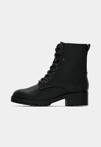Bottines noires en cuir lisse, avec un design à lacets, un bout rond, une semelle épaisse et un talon carré. Les accents comprennent des œillets et une languette.