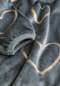 Fleece blanket in dark gray with metallic gold heart pattern. Soft texture, featuring a ribbed edge on one side for added detail.