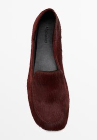 Scarpa slip-on color bordeaux realizzata in materiale morbido e testurizzato con interno liscio nero. Presenta una punta arrotondata e dettagli di cuciture minime.