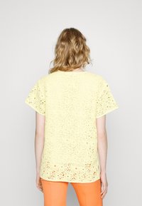 Haut à manches courtes en dentelle jaune pâle avec motifs floraux, col rond et ourlet festonné. Associé à un pantalon orange.