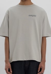 Camiseta oversized de color gris claro, hecha de algodón suave, con un pequeño logo bordado en el pecho y un escote redondo.