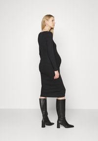 Vestido bodycon preto de manga longa com comprimento midi, apresentando uma textura suave. Combinado com botas pretas de salto alto até ao joelho.