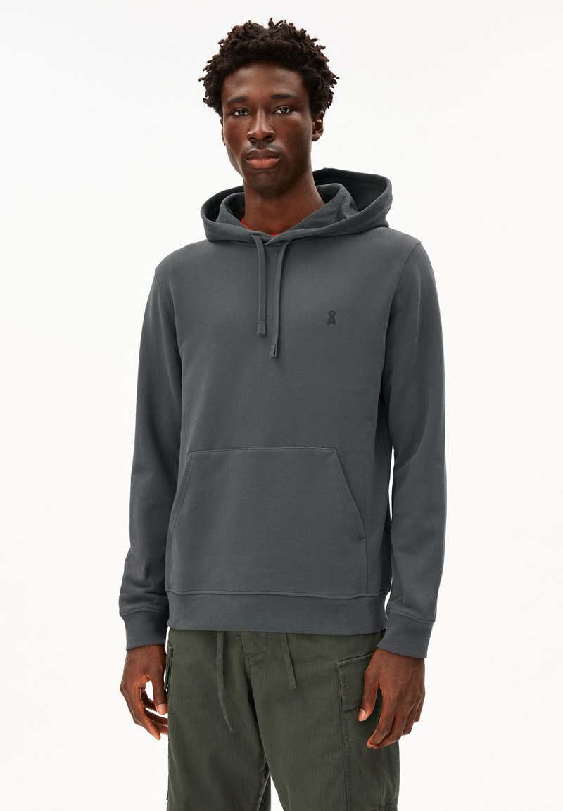 Felpa con cappuccio grigia scura in tessuto morbido, con tasca a canguro, cappuccio con coulisse e logo discreto sul petto. Abbinata a pantaloni verde oliva.