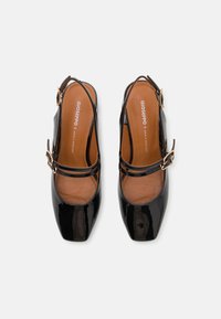 Musta lakattu nahka slingback-kengät neliönmuotoisella kärjellä, nilkkahihnalla ja kultasävyisellä soljella. Ruskea nahkasisäpohja, jossa on tikkaukset.