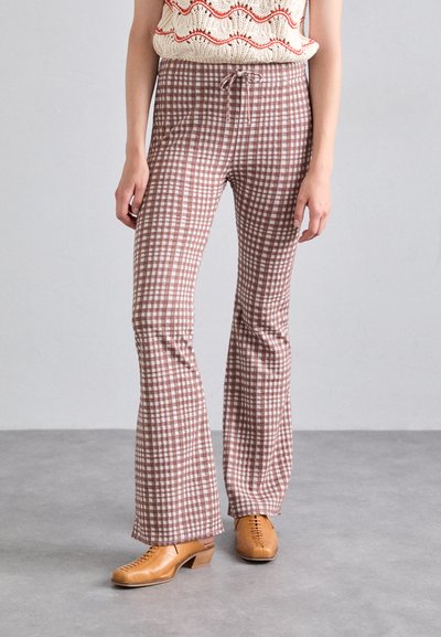 Brune og hvide gingham flared bukser med snor i livet, parret med beige snørebåndsko, på en model mod en ensfarvet baggrund.
