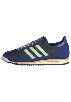 Baskets Adidas discrètes bleu marine avec des rayures vert menthe, une semelle intermédiaire marron clair et une semelle extérieure noire texturée.