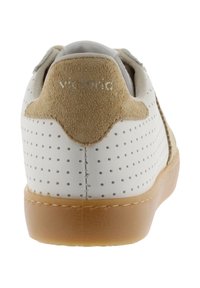 Zapatilla blanca con lados perforados, lengüeta trasera de ante beige, suela marrón claro y costuras visibles en la parte trasera.