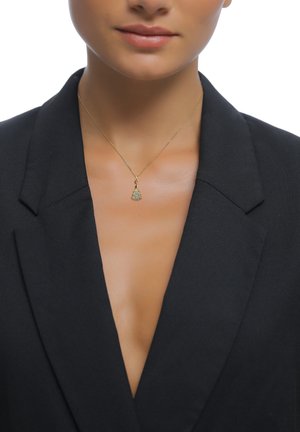 Guldhalsband med ett dekorativt hänge med turkosa detaljer, bärs över en svart kavaj. Närbild som framhäver smyckets detaljer.