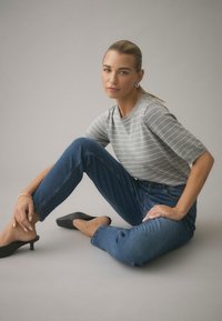 Grårandig kortärmad topp kombinerad med blå jeans och svarta mule-skor med klack. Outfiten har en avslappnad passform och enkla designelement.