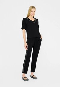 Svart T-shirt med V-ringning och korta ärmar, med metalliska logodetaljer. Matchas med svarta sweatpants med logodetaljränder.