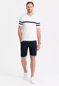 Camisa polo blanca con rayas marinas, pantalones cortos de mezclilla azules, zapatillas blancas, mangas cortas, corte casual y dobladillo enrollado en los pantalones cortos.