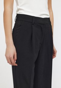 Zwarte op maat gemaakte broeken met een hoge taille, voorzien van plooien, zijzakken en een gladde stoftextuur. Fitted, rechte pijpen.