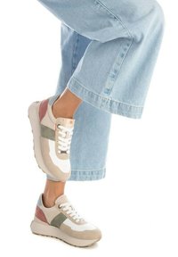 Zapatillas beige y blancas con detalles en verde y rosa, fabricadas en tejido texturizado, con suela plana, cordones y un cuello acolchado. Combinadas con unos vaqueros de pierna ancha en azul claro.