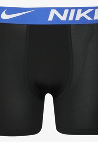 Zwarte atletische boxershorts met een blauwe elastische tailleband waarop het Nike-logo in het wit staat. Gladde textuur, aansluitend ontwerp en een middellange snit.