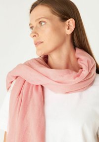 Écharpe en tricot rose drapée autour du cou, présentant une texture douce et un design ample et décontracté. Portée sur une chemise blanche.