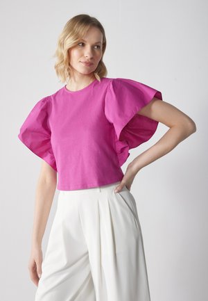 Short pink puff-sleeve top made of cotton, featuring a round neckline and a cropped design, paired with white wide-leg trousers.