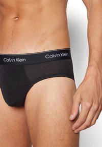 Fekete pamut alsónadrág, fehér "Calvin Klein" márkázású derékrésszel, amely kényelmesen illeszkedik és sima tapintású.