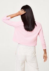 Jersey corto de color rosa claro con mangas tres cuartos, combinado con pantalones blancos a rayas. Textura suave sin patrones ni adornos visibles.