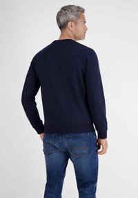 Dunkelblaues Baumwoll-Sweatshirt mit langen Ärmeln, rundem Hals, Rippbündchen und Saum, kombiniert mit blauen Jeans, von hinten betrachtet.