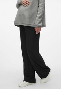 Pantalons larges noirs à côtes avec une taille élastique, fabriqués en un matériau doux, associés à un sweatshirt gris surdimensionné et des baskets blanches.