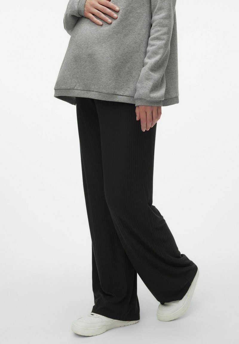Pantalons larges noirs à côtes avec une taille élastique, fabriqués en un matériau doux, associés à un sweatshirt gris surdimensionné et des baskets blanches.