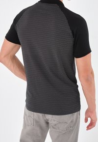 Polo shirt noir à manches courtes et à motifs, avec un design texturé au dos, des manches unies contrastantes et une coupe ajustée.