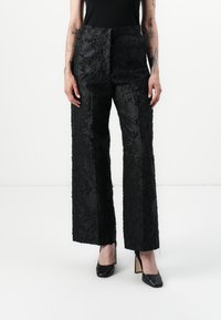 Black floral-embroidered wide-leg trousers with a matte finish. Features a flat waistband and a textured pattern. Paired with black heels.