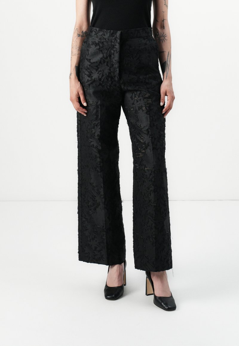 Black floral-embroidered wide-leg trousers with a matte finish. Features a flat waistband and a textured pattern. Paired with black heels.