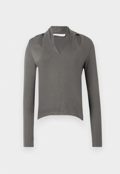 Harmaa pitkähihainen paita, jossa on syvä V-pääntie, lyhennetty malli ja leikattuja olkapäitä. Valmistettu pehmeästä ja sileästä kankaasta. Sauma keskellä edessä.