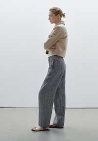 Beige cropped leather jacket, gray wide-leg trousers, and black sandals. Smooth texture with visible seams and pleats in the trousers.