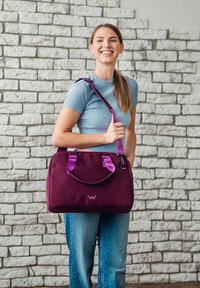 Bordeauxfarbene Schultertasche mit lila Trägern, aus strapazierfähigem Stoff gefertigt, mit zwei Griffen, Reißverschluss und einem geprägten Logo auf der Vorderseite.