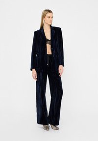 Traje de terciopelo en azul marino oscuro, que incluye una americana ajustada y pantalones de pierna ancha. La tela tiene una textura acanalada y un ligero brillo.