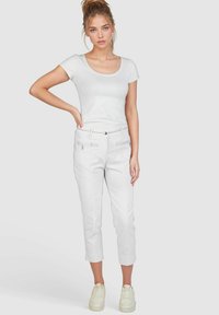 Weißes, eng anliegendes T-Shirt und weiße, cropped Hose mit Taschen. Das Outfit zeichnet sich durch einen subtilen Glanz, einen geraden Schnitt und umgeschlagene Bündchen aus, kombiniert mit hellen Sneakers.