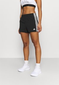Shorts deportivos negros con una cintura elástica, que presentan tres rayas blancas a los lados y un logo de Adidas en el dobladillo inferior.