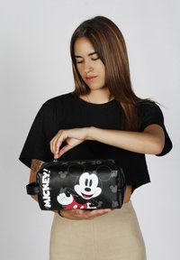 Trousse de maquillage noire avec graphisme de Mickey Mouse, accents rouges et fermeture éclair à crochet. Présente un design rectangulaire et une poignée latérale.