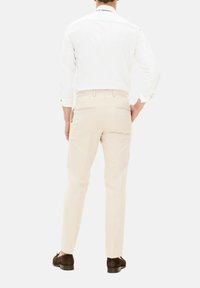 Pantaloni beige chiaro con una vestibilità su misura, dotati di tasche posteriori e texture sottili, abbinati a una camicia bianca a maniche lunghe e scarpe marroni.