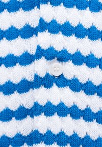 Κοντινή λήψη υφάσματος με μπλε και άσπρο ζιγκ-ζαγκ πλέξιμο, με ένα λευκό κουμπί τεσσάρων τρυπών ραμμένο στο κέντρο.