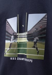 La camiseta navy presenta un estampado gráfico de un campo de rugby con dos jugadores en acción. Texto "Campeonatos IKKS" en blanco debajo del diseño.