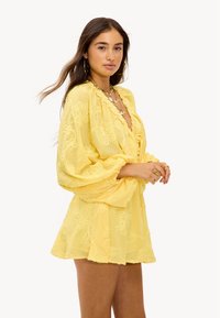 Robe jaune à motif floral avec un décolleté en V, des manches bouffantes et une jupe évasée. Confectionnée en tissu texturé et léger.