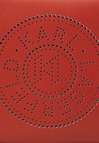 Red leather product featuring perforated design with black accents, displaying the text "KARL" in a circular pattern. Textured surface.